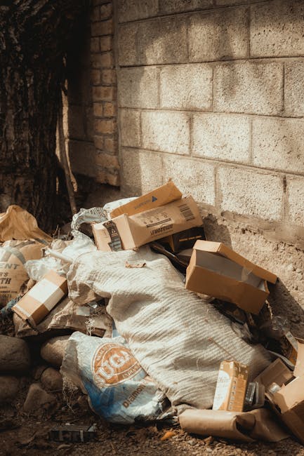 A close-up image of three black plastic rubbish bags, tightly knotted at the top, resting against a plain, light-colored wall, likely on a pavement or driveway. The bags appear to be made of glossy, crinkled plastic material, with reflective surfaces catching some ambient light. The focus is on the bags in the foreground, with their textures and creases prominently detailed, while the background is neutral and blurred, providing no additional environmental context. The scene suggests a typical setting for waste awaiting collection or disposal, linked to private waste handling services like those offered by Waste Disposal Finchley. The professional environment underscores the importance of proper rubbish management, especially in a domestic or commercial context that may opt for independent collection or on-site clearance, avoiding reliance on local authority refuse disposal. Overall, the image captures the mundane yet essential aspect of rubbish removal in an urban or suburban setting, suitable for service-related content focused on alternative waste disposal solutions.